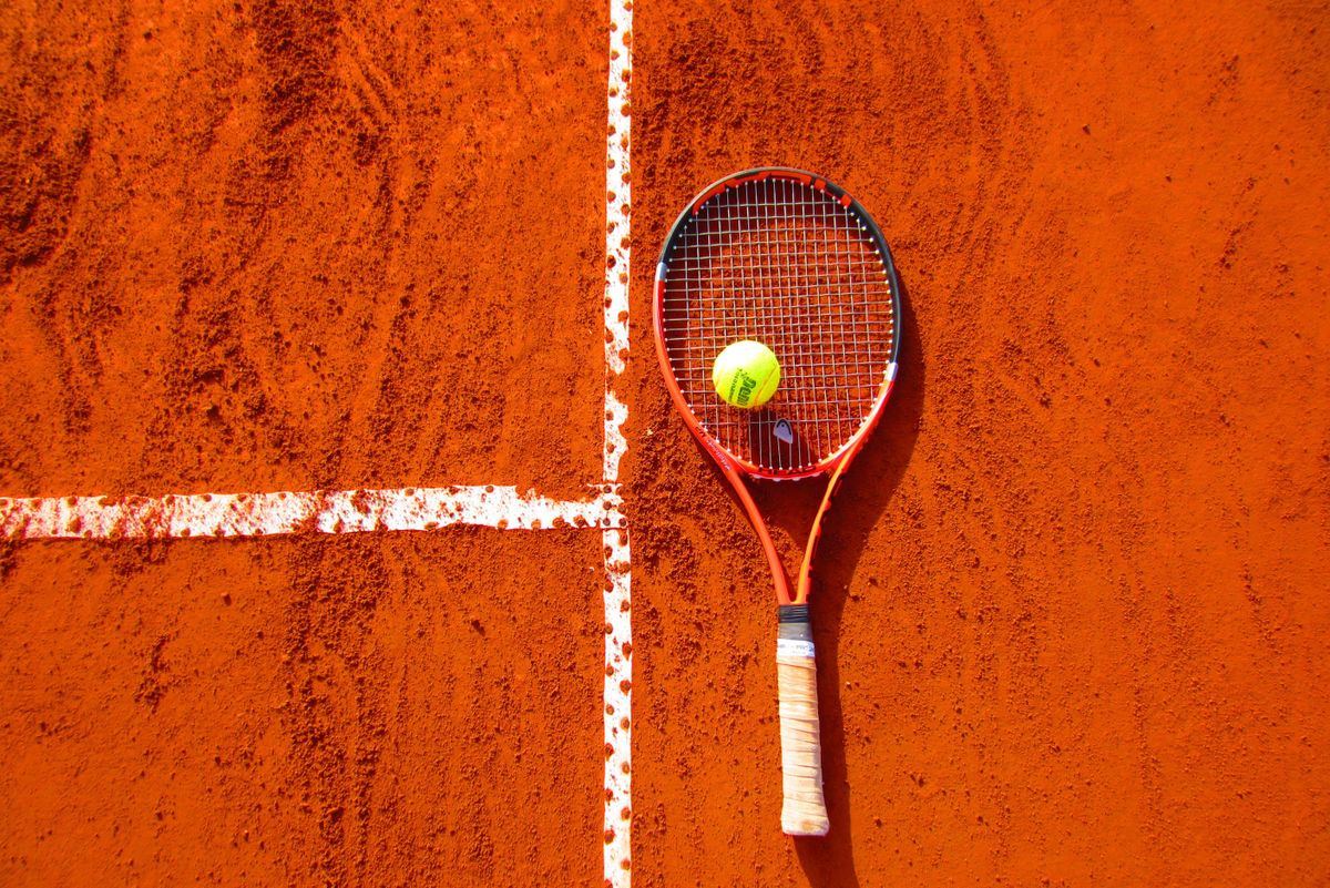 Tennisschläger mit Ball liegt auf einem Sandplatz an der Linie