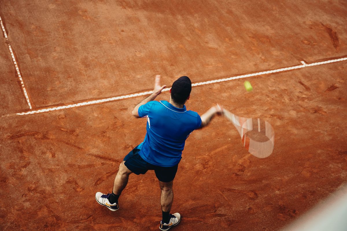 Tennisspieler beim Vorhandschlag auf einem Sandplatz, von schräg oben